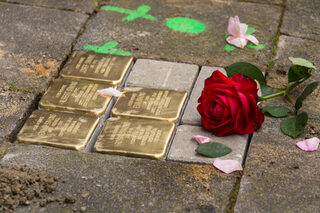 Fünf neue Stolpersteine mit blitzendem Messing, eine Markierung und noch Reste von Sand und Zement. Daneben wurde eine rote Rose und einige rosa Blütenblätter gelegt