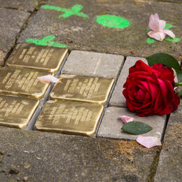 Fünf neue Stolpersteine mit blitzendem Messing, eine Markierung und noch Reste von Sand und Zement. Daneben wurde eine rote Rose und einige rosa Blütenblätter gelegt